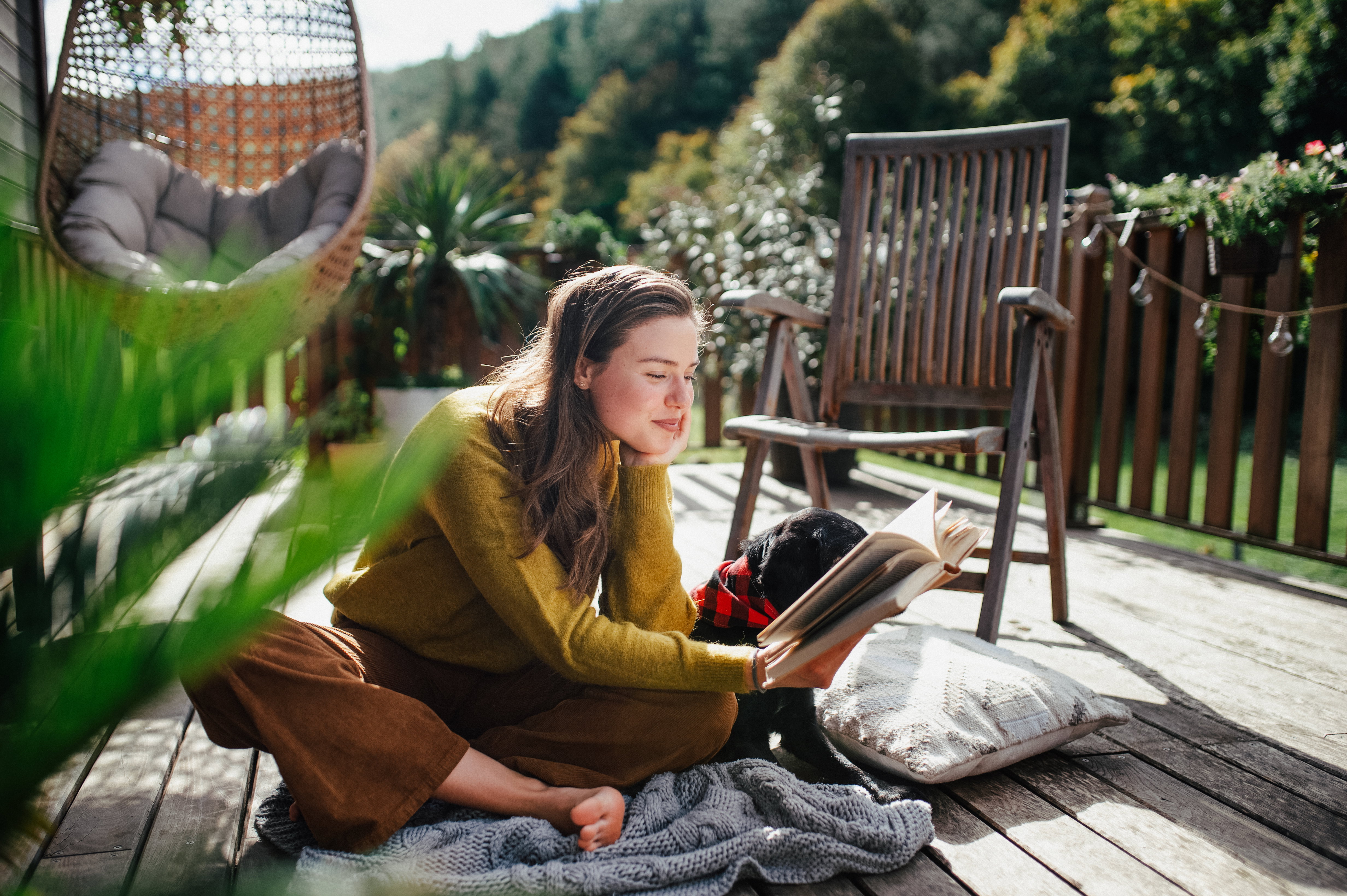 Woman sitting on patio with dog, reading book. Portrait of beautiful woman.