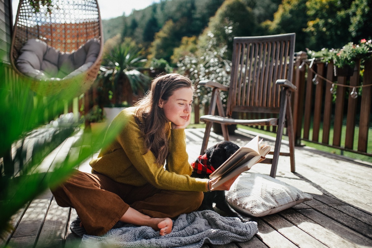 Woman sitting on patio with dog, reading book. Portrait of beautiful woman.