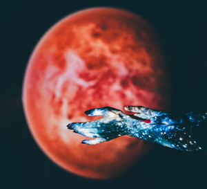 A close-up shot of two hands, projected with a vibrant blue galaxy pattern, are posed against a blurred red planet backdrop.