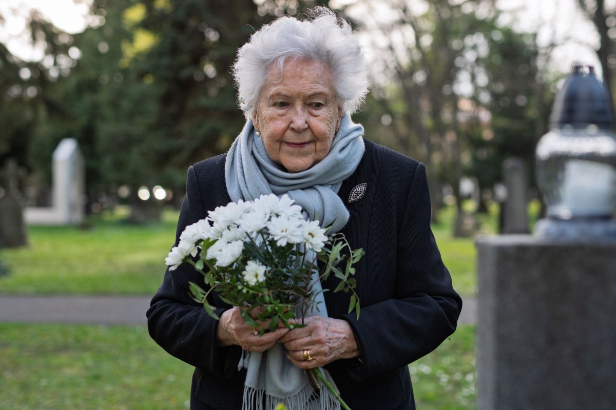Starsza kobieta z kwiatami na cmentarzu