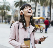Spain, Barcelona, laughing woman with coffee, cell phone and headphones in the city
