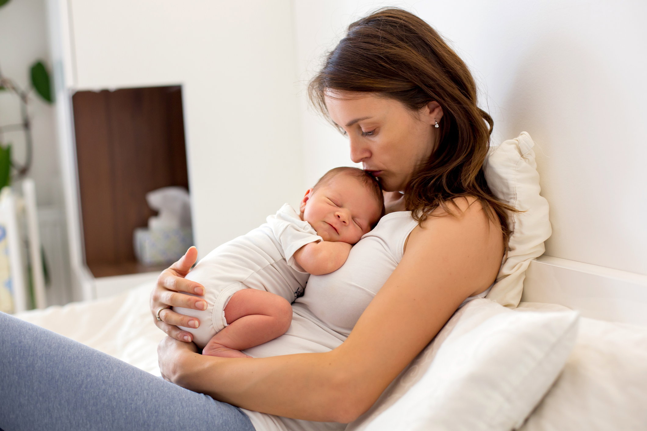 Young mother lying in bed with her newborn baby boy