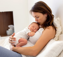Young mother lying in bed with her newborn baby boy