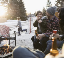 Family roasting marshmallows and drinking beer at fire pit in snowy driveway