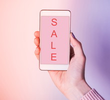 Close-Up Of Woman Hand Holding Mobile Phone Showing Sale Text Against Colored Background