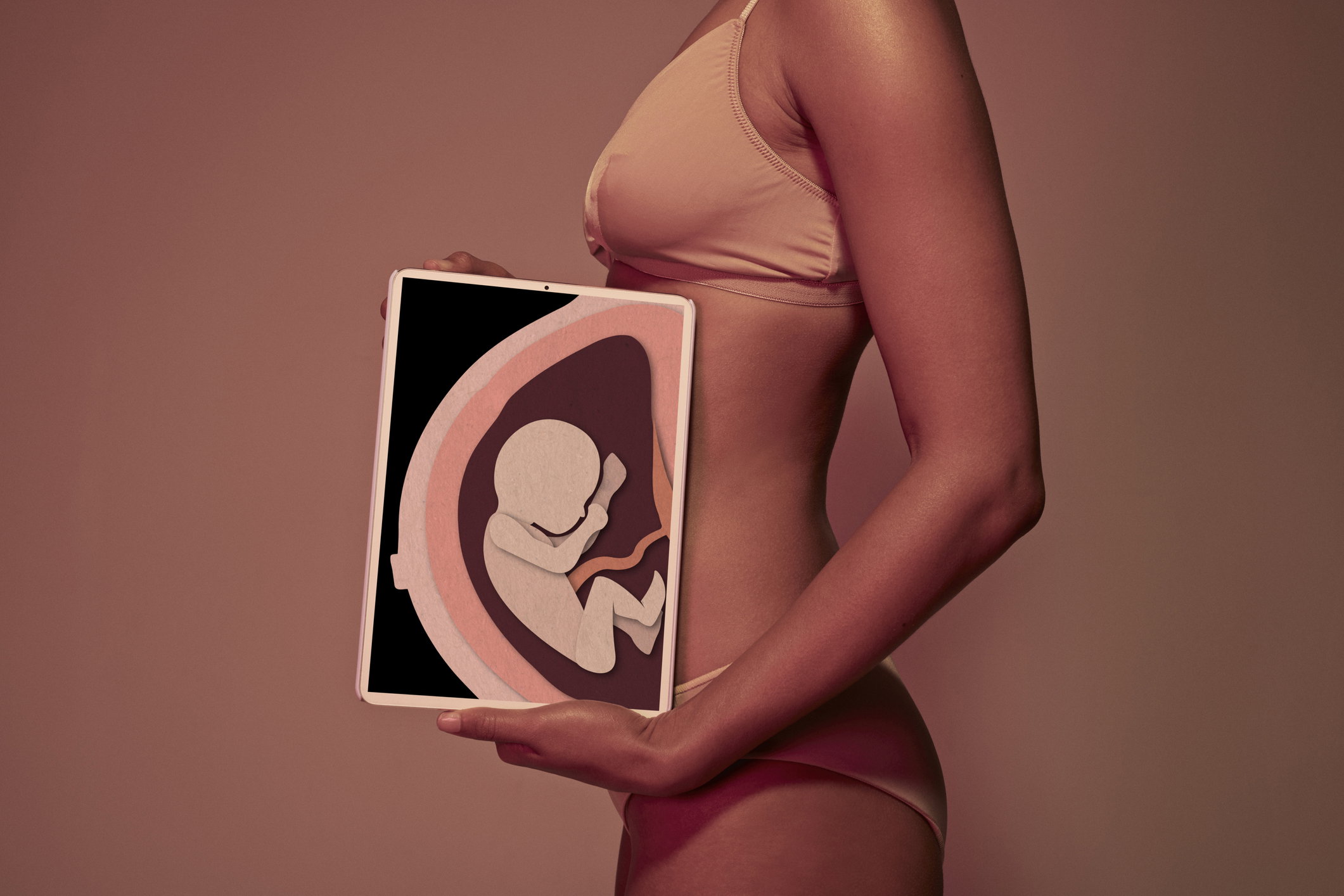 Pregnant young woman holding tablet in front of belly to display baby