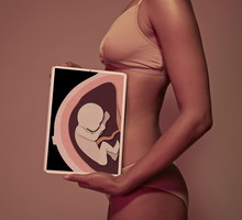 Pregnant young woman holding tablet in front of belly to display baby