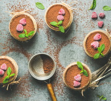 Homemade Italian dessert Tiramisu served in individual glasses with mint leaves, raspberries and cocoa powder over grey concrete background