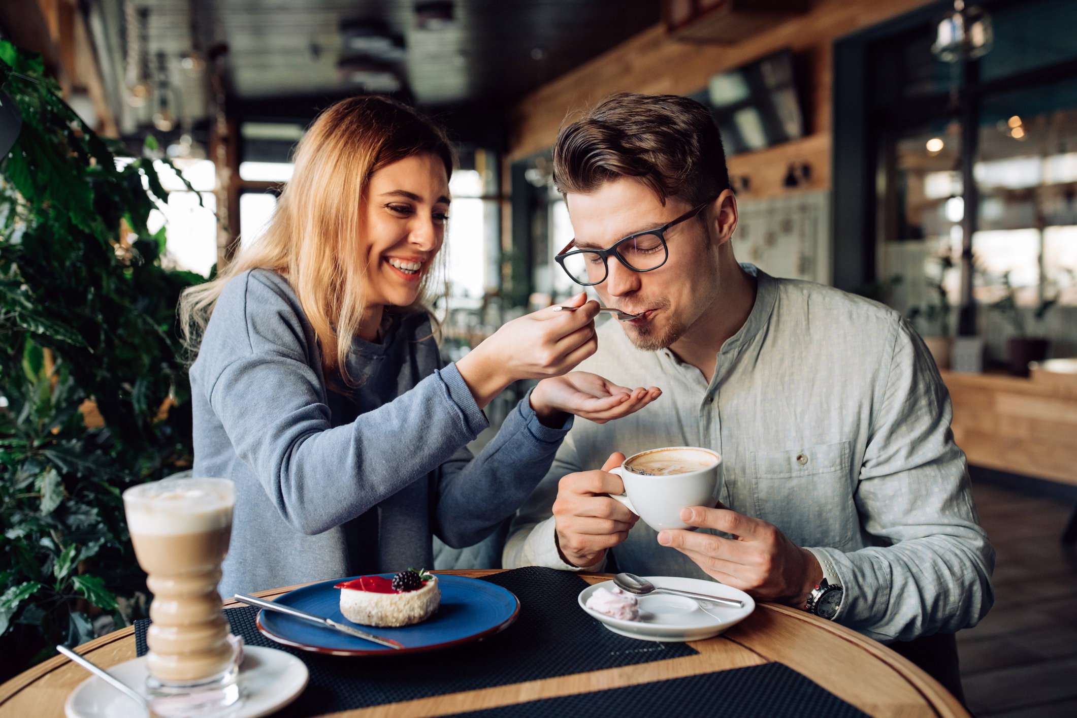 Cheerful girl feeding her boyfriend, while resting at cafe