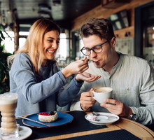 Cheerful girl feeding her boyfriend, while resting at cafe