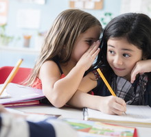 Girl whispering to classmate in school