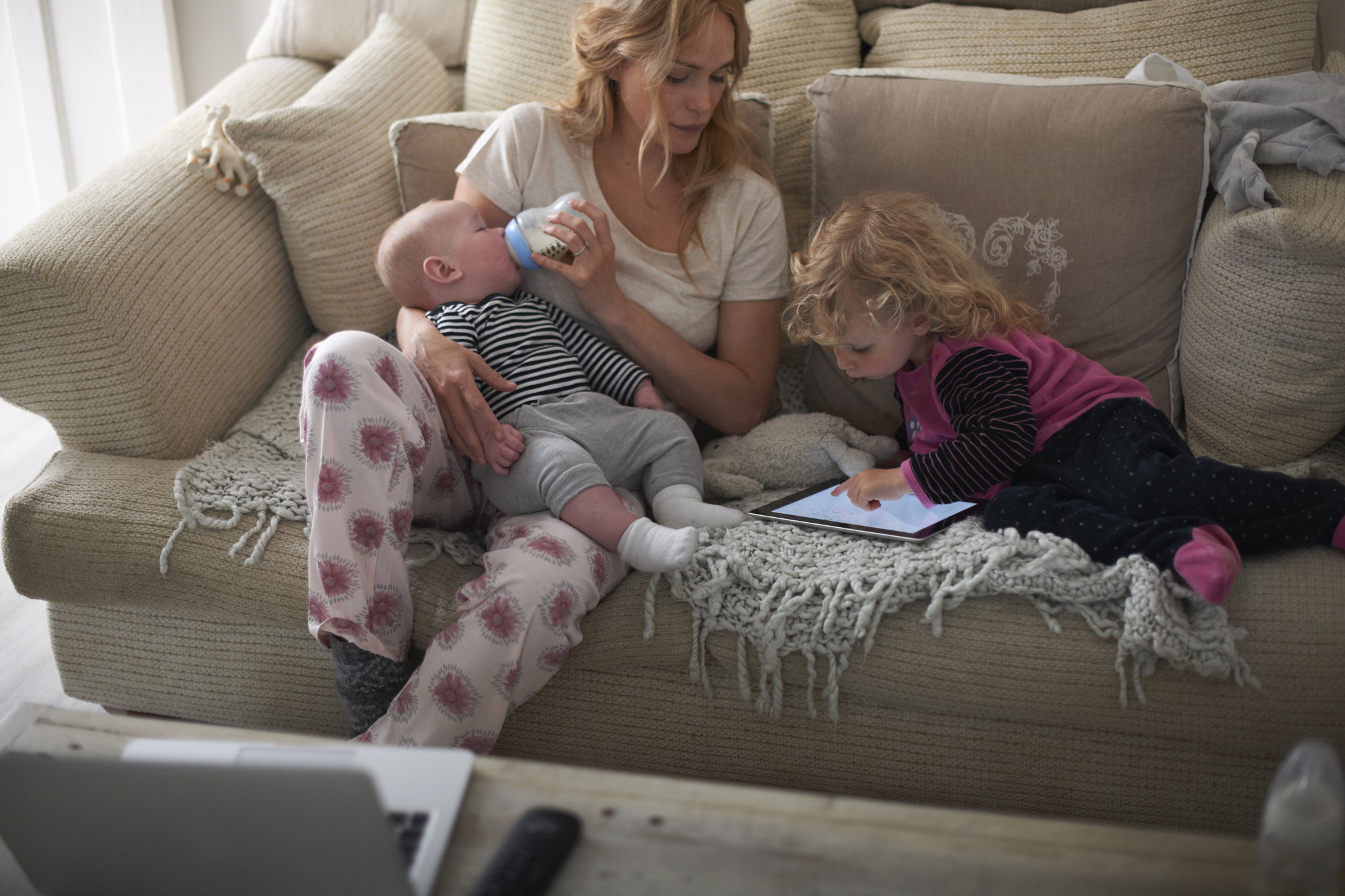 Mother feeding baby son and helping daughter with digital tablet