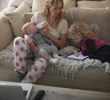 Mother feeding baby son and helping daughter with digital tablet