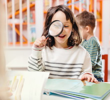 girl smiling reading book with magnifying glass