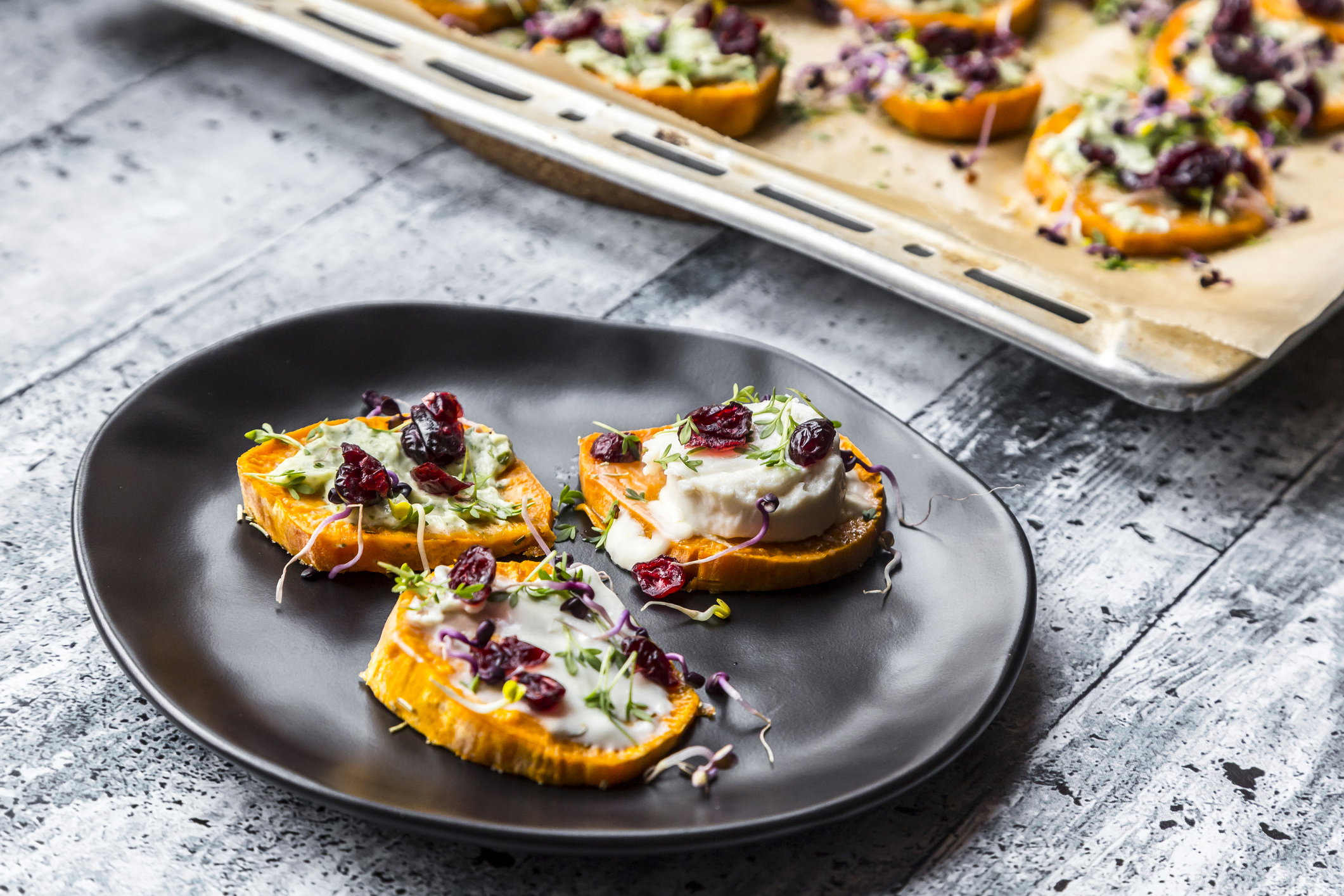 Slices of sweet potato with cream cheese, ramson cream, goat cheese, cress and cranberries