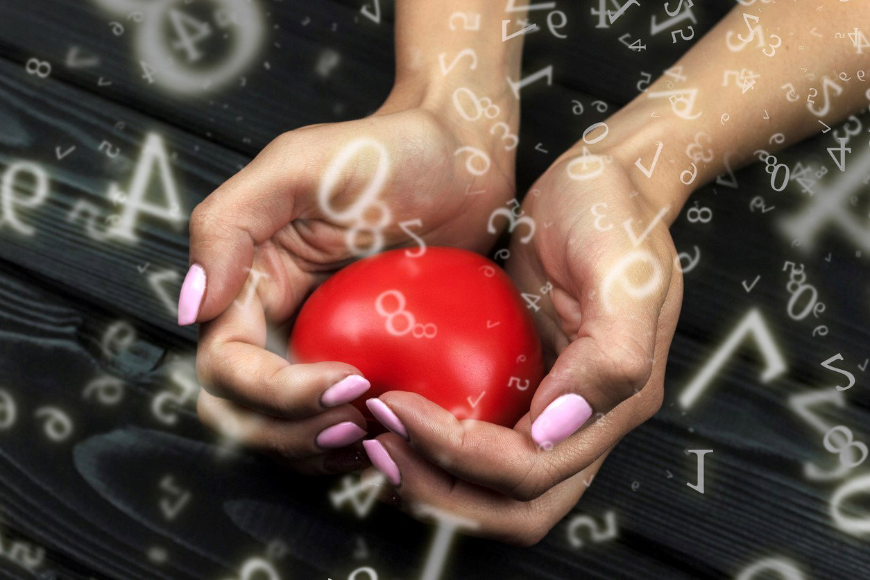 numerology, red heart clamped in female hands on a black wooden background surrounded by numbers