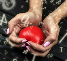numerology, red heart clamped in female hands on a black wooden background surrounded by numbers