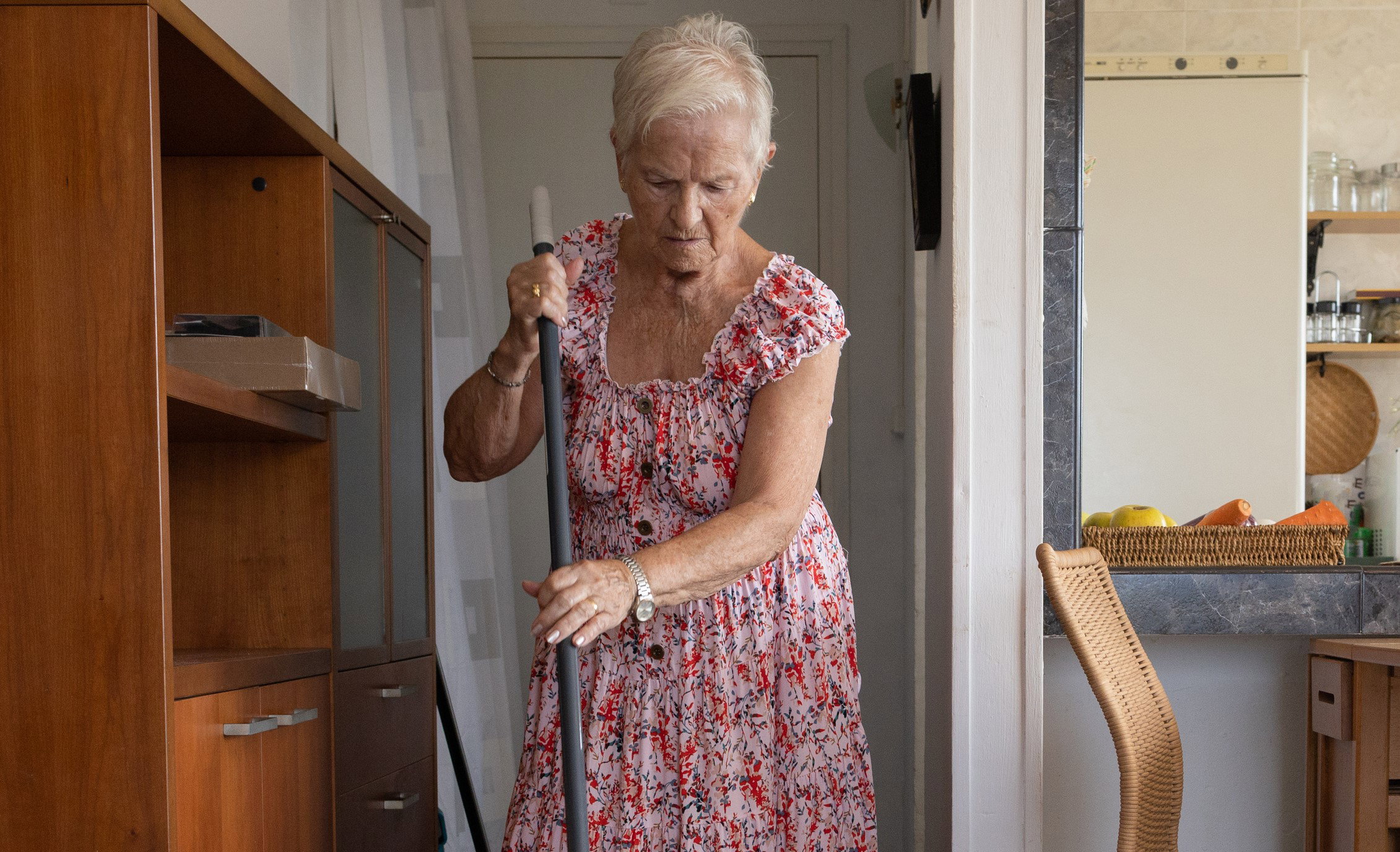 elderly gray-haired woman sweeping the floor with a broom at home.80-year-old independent woman