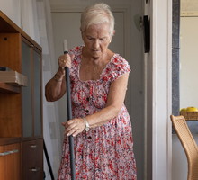 elderly gray-haired woman sweeping the floor with a broom at home.80-year-old independent woman