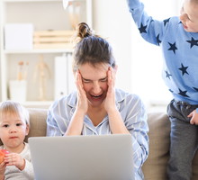 Stressed and frustrated mother with two small children in pajams working in home office, quarantine concept.