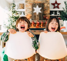 Boy and girl sitting at the dining table messing about at Christmas
