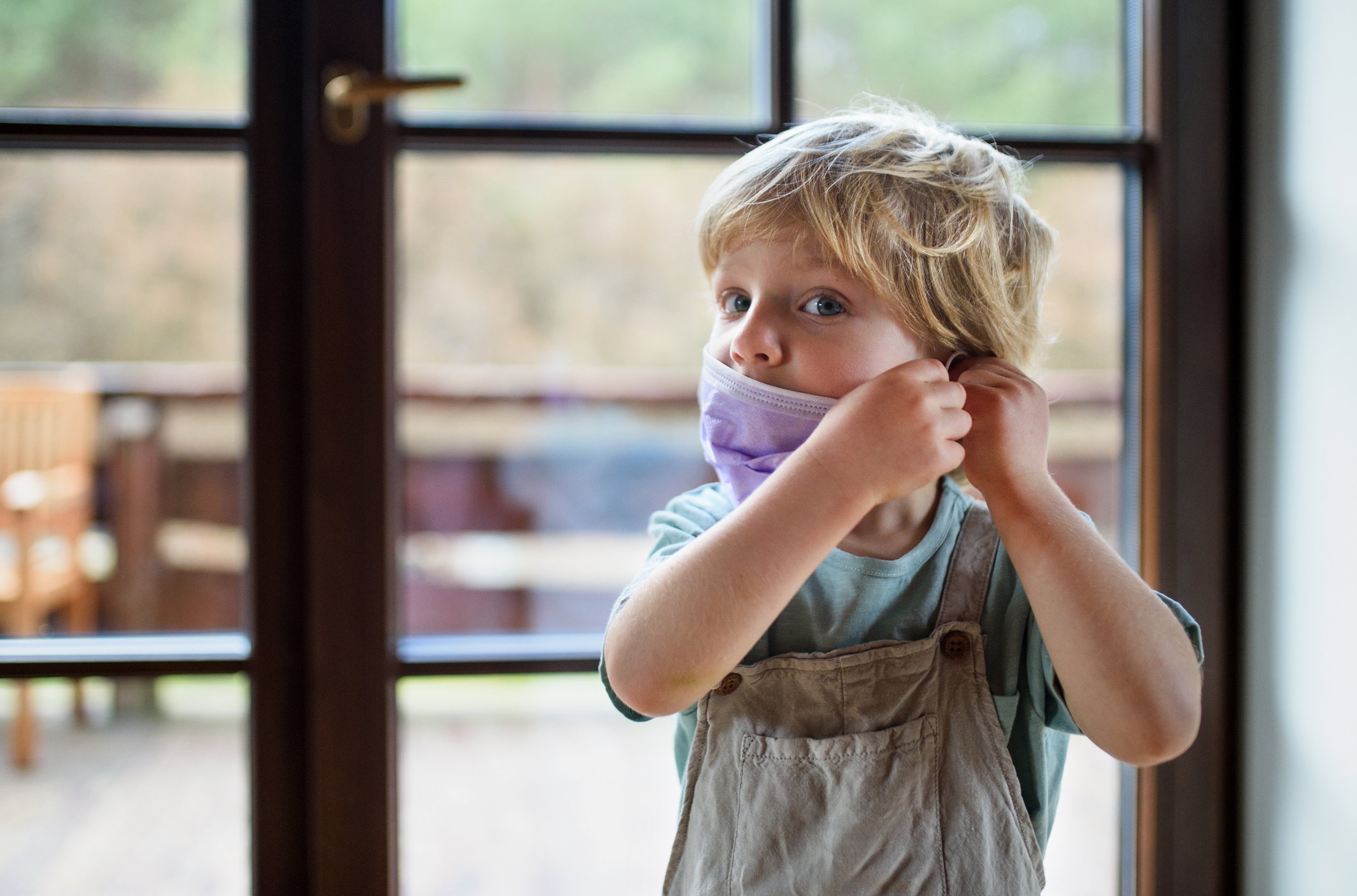 Front view of unhappy small boy with face mask at home.