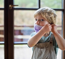 Front view of unhappy small boy with face mask at home.