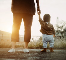 Low section of mother holding baby daughter's hand walking in the park and enjoying the beautiful sunset
