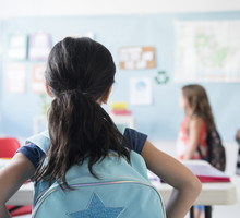 Girl in classroom wearing backpack watching classmates