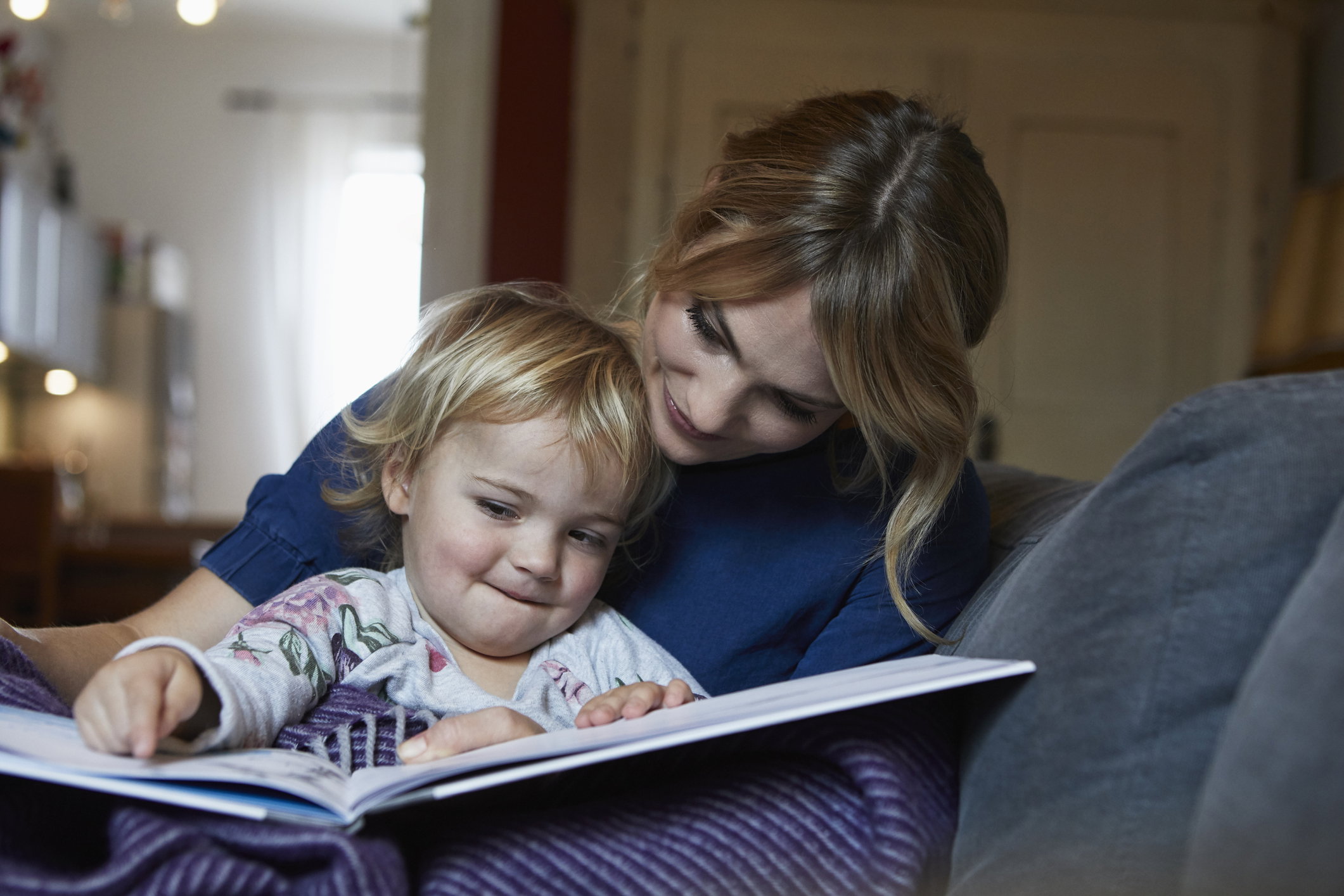 Mother and little daughter sitting on the couch at home watching book