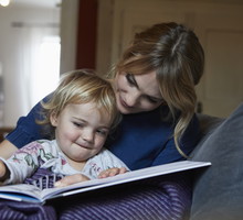 Mother and little daughter sitting on the couch at home watching book