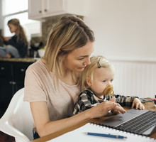 Mid adult woman using laptop while daughter sitting on her lap at home