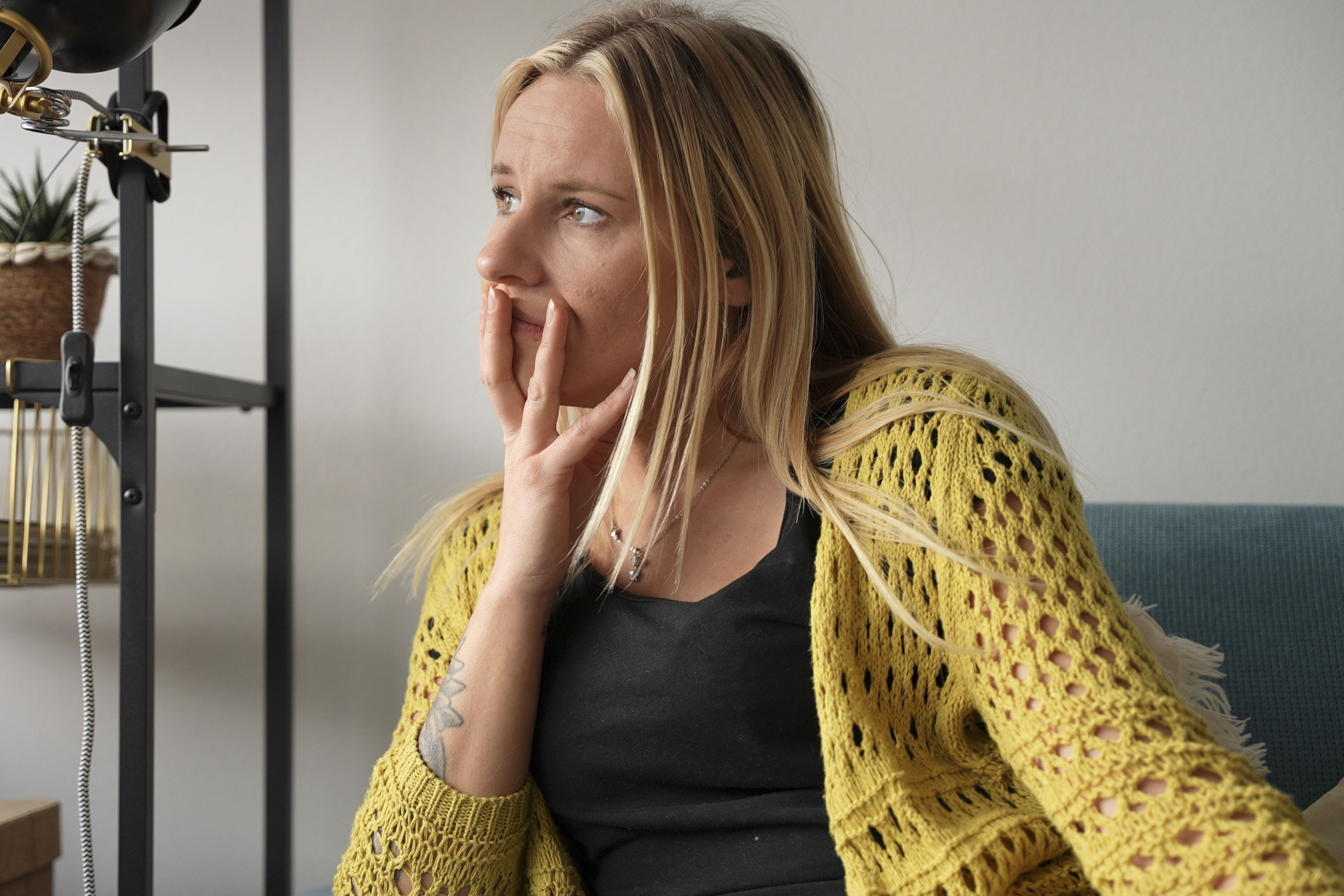 Pensive Young Woman Sitting on Sofa Looking Away Touching Face with Hand