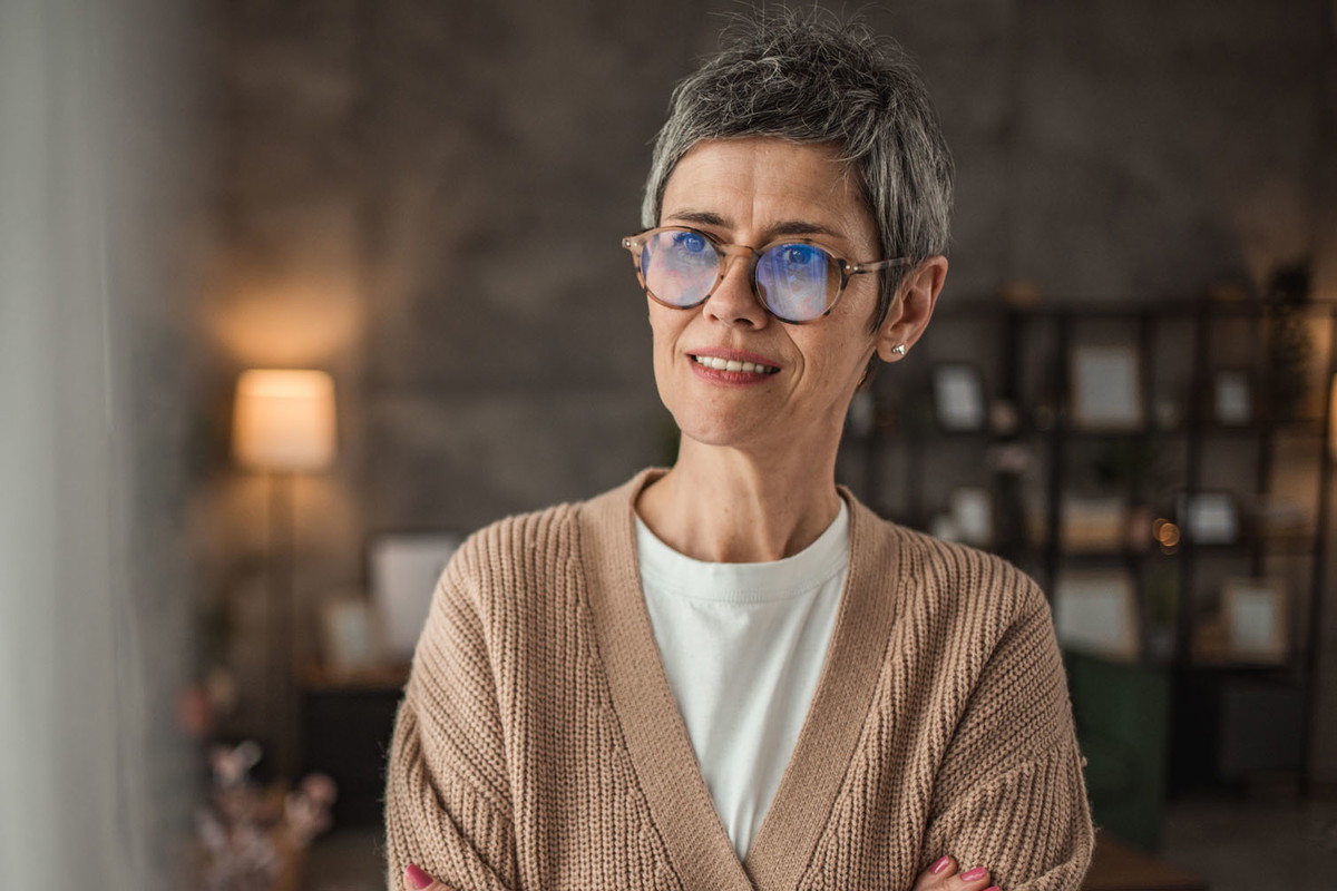 Portrait of a mature woman with gray short hair and casual clothes standing in a room.
