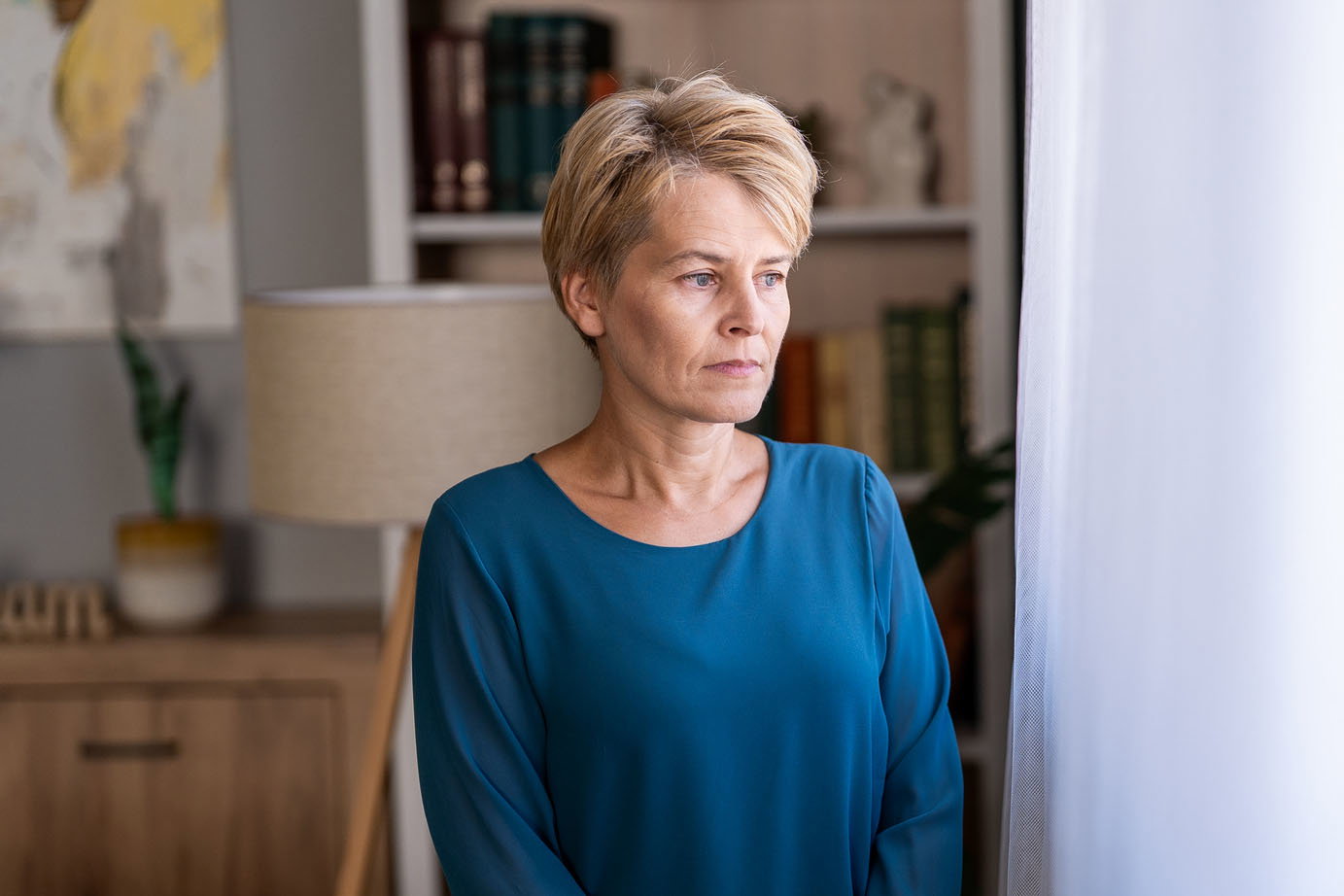 Mature woman standing alone at home feeling thoughtful and sad