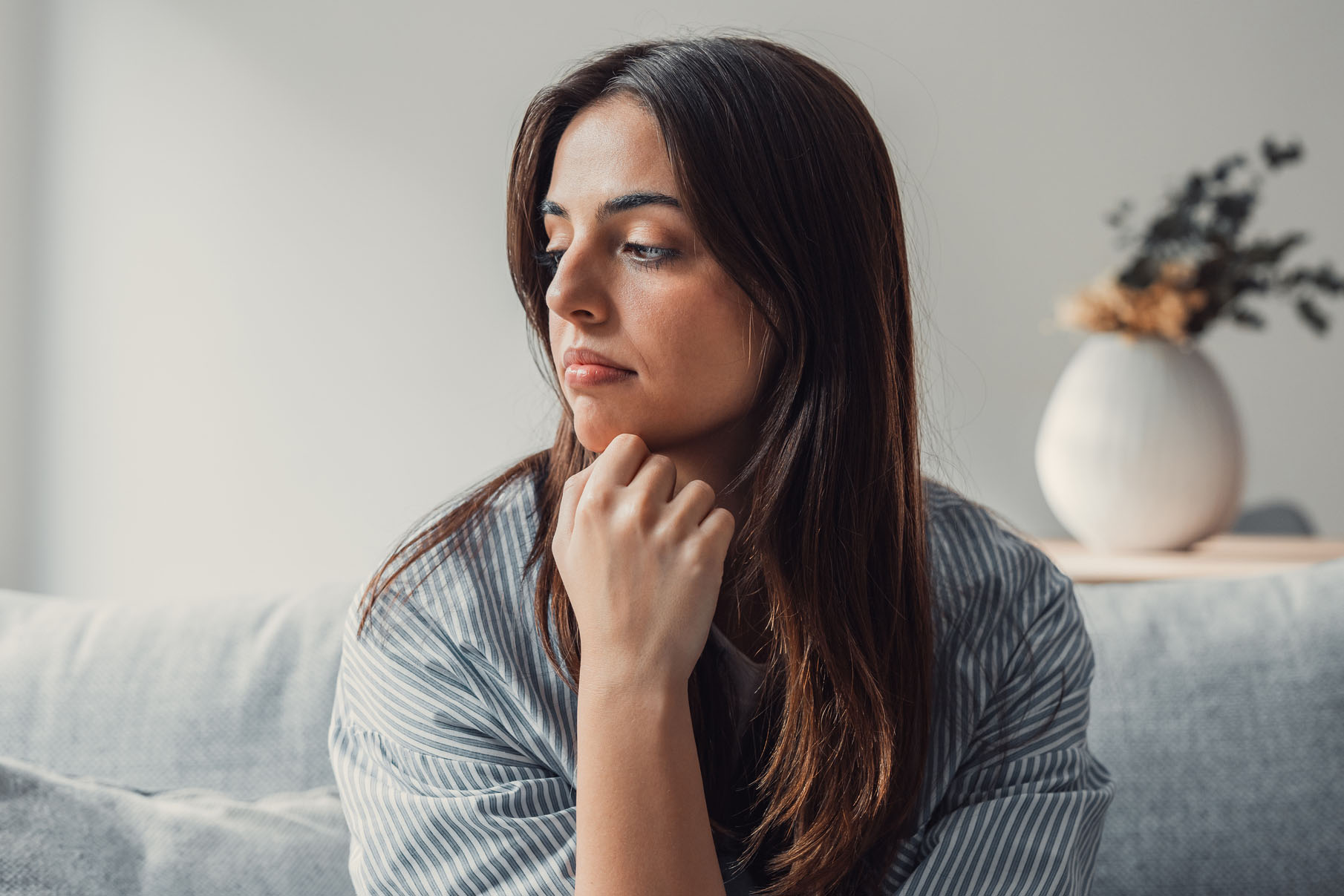 Close up of sad pensive millennial woman sit alone thinking about relationships personal problems, upset thoughtful young female lost in thoughts feel lonely depressed pondering or mourning at home