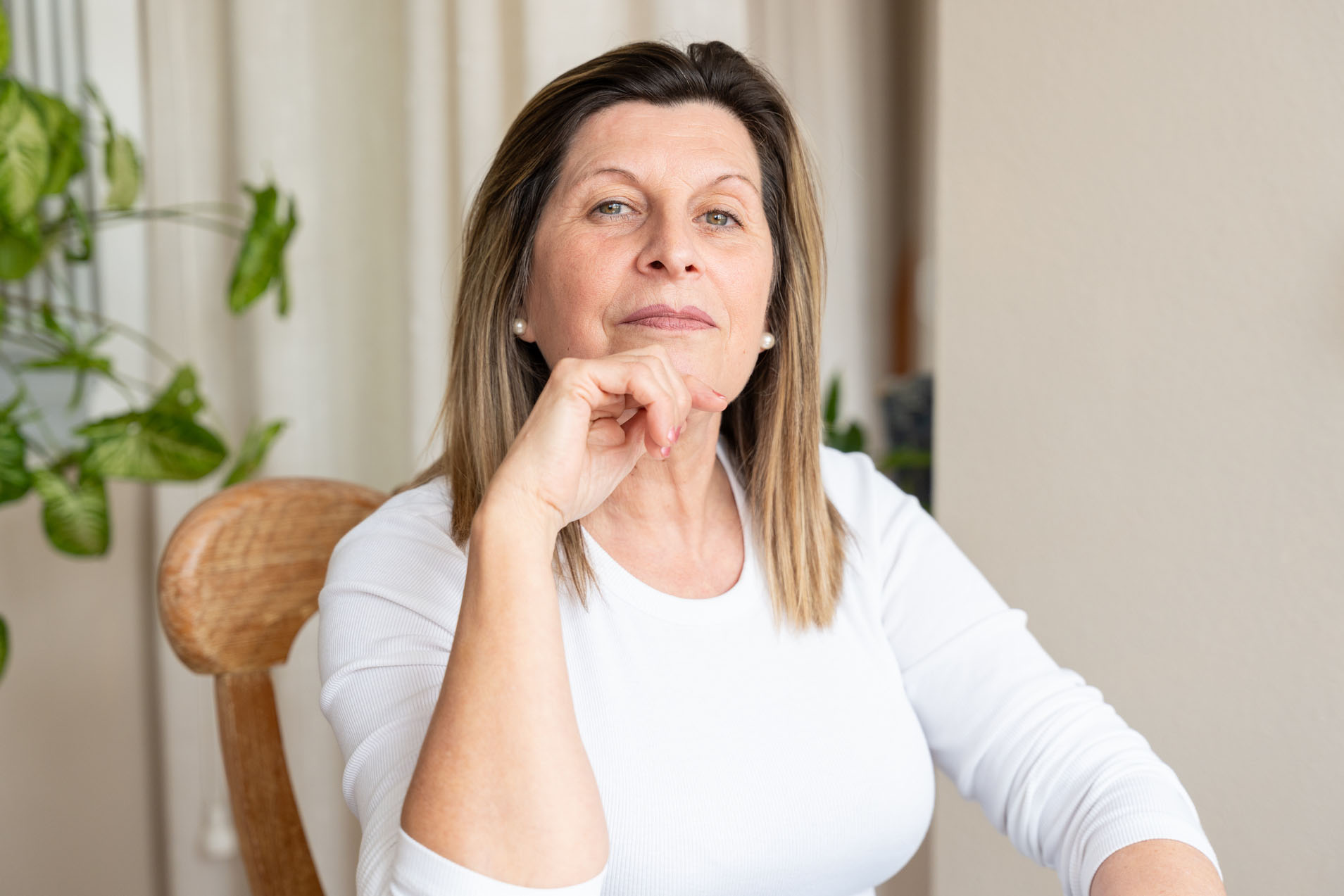 Mature adult woman at home, sitting and looking at camera. She is thinking and enjoying quiet moment during the day