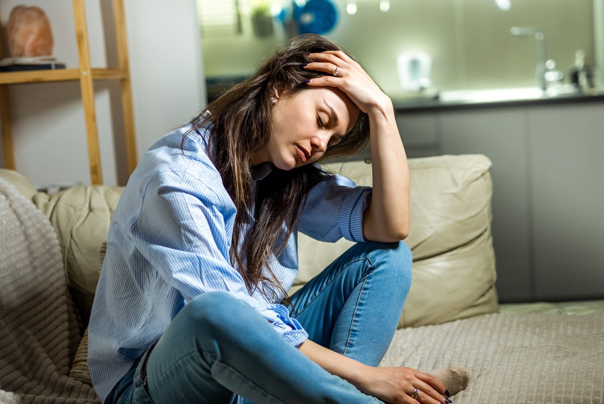 kobieta w wieku 30 plus siedzi na kanapie na tle kuchni zupełnie załamana