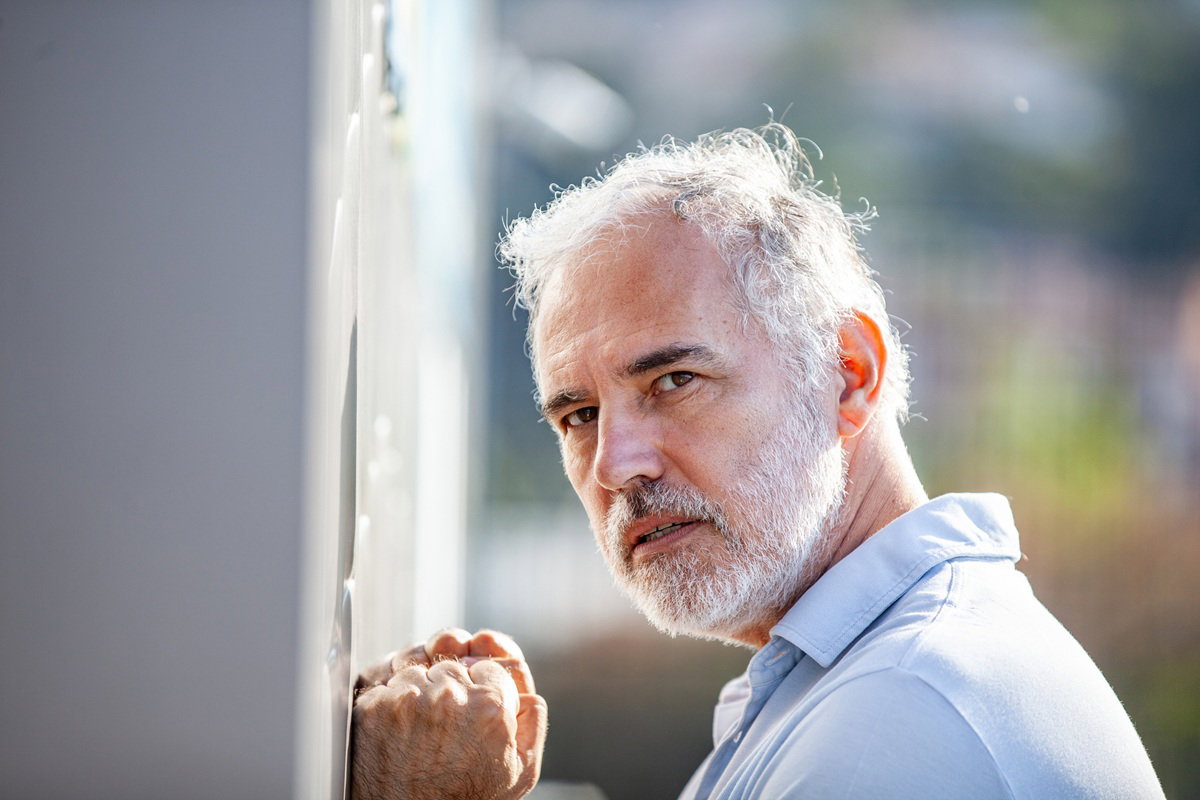 mężczyzna w wieku 50 lat siwy i łysiejący z zarostem stoi przy ścianie zmartwiony