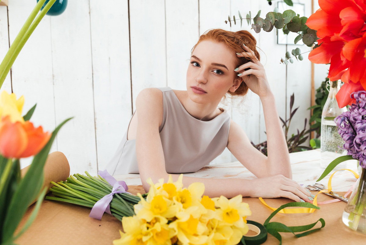 kobieta w wieku 25 plus siedzi przy stole z kwiatami w kwiaciarni zamyślona