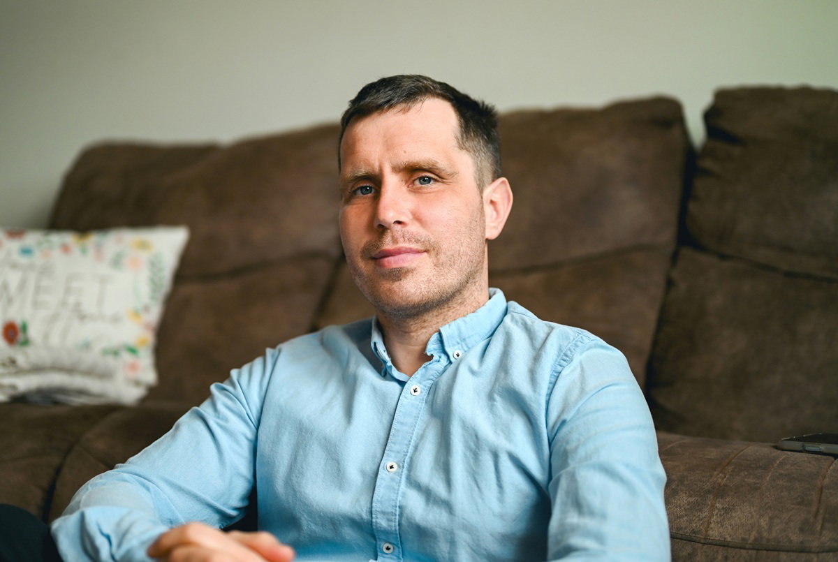 mężczyzna w wieku 30 plus w jasnej koszuli siedzi na ziemi przed kanapą i patrzy przed siebie