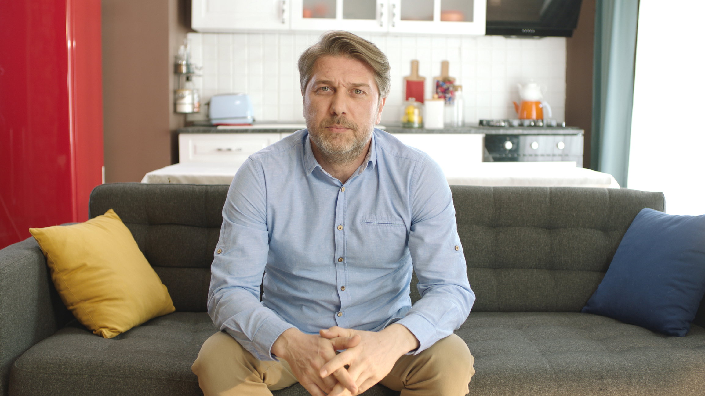Young man looking nervously at camera while sitting on sofa at home.