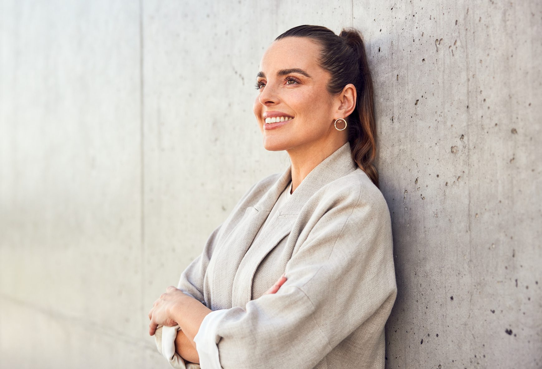 Adult successful businesswoman daydreaming looking up standing against concrete wall in urban scene