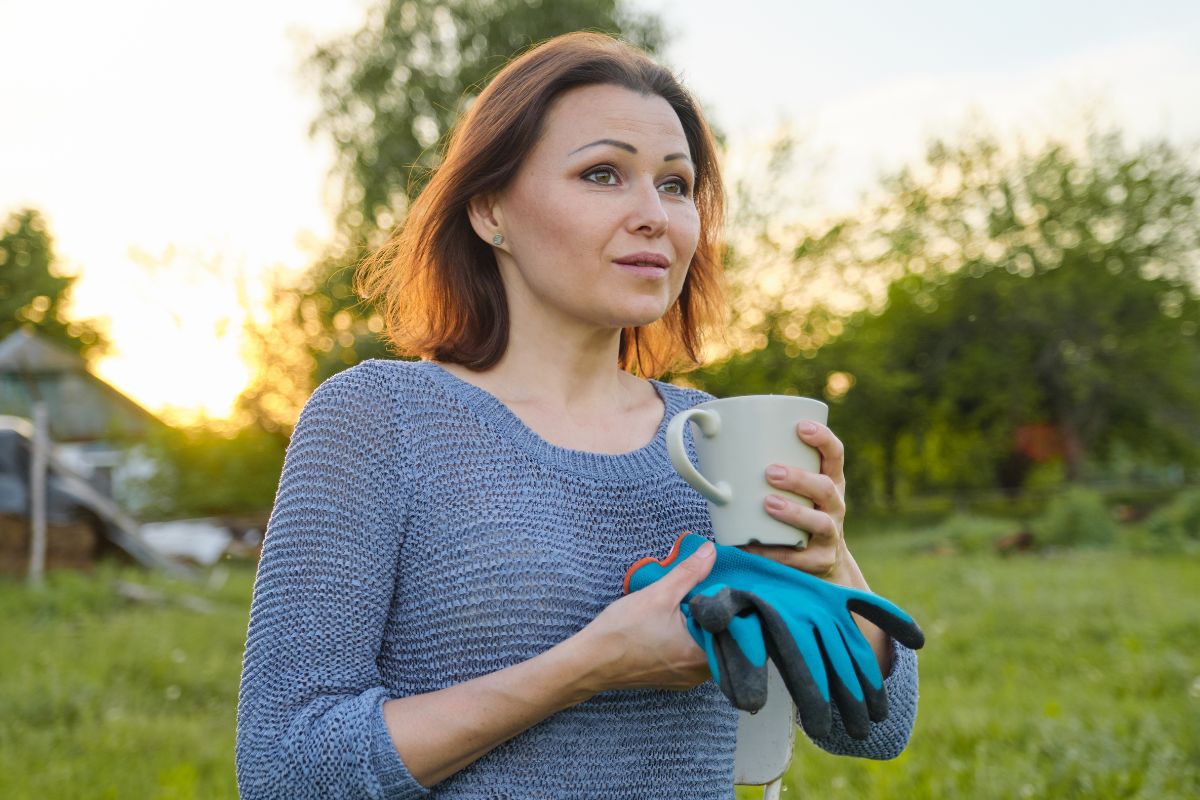 Kobieta z rękawicami i kubkiem w ogrodzie