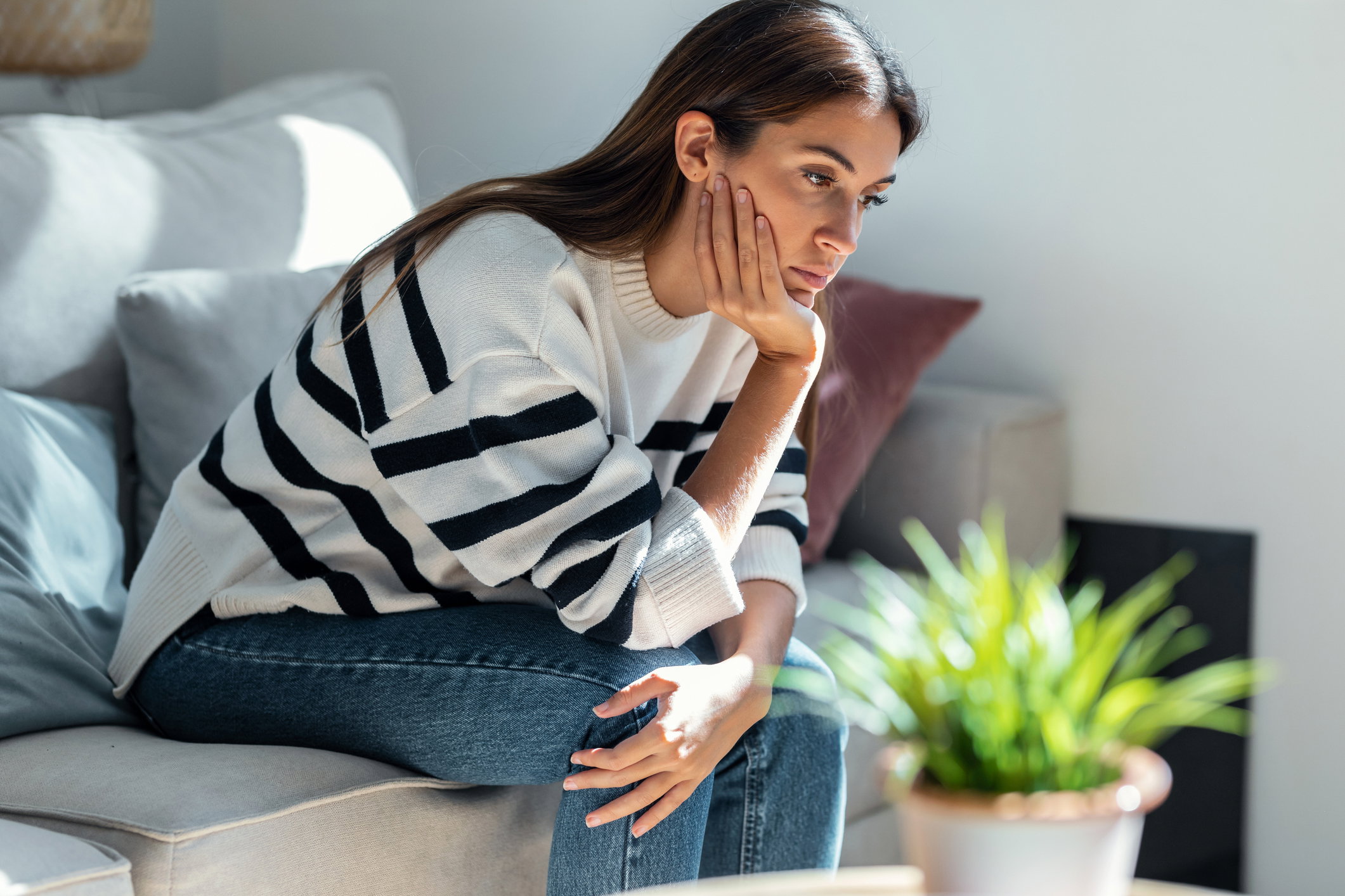 Depressed young woman thinking about her problems while sitting on the sofa at home.