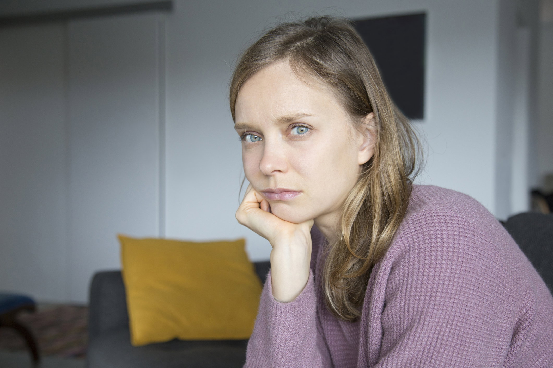 Upset young woman sitting on sofa at home, looking at camera