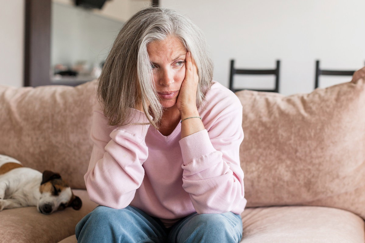 Sad pensive middle age woman looking down depressed sitting on the sofa