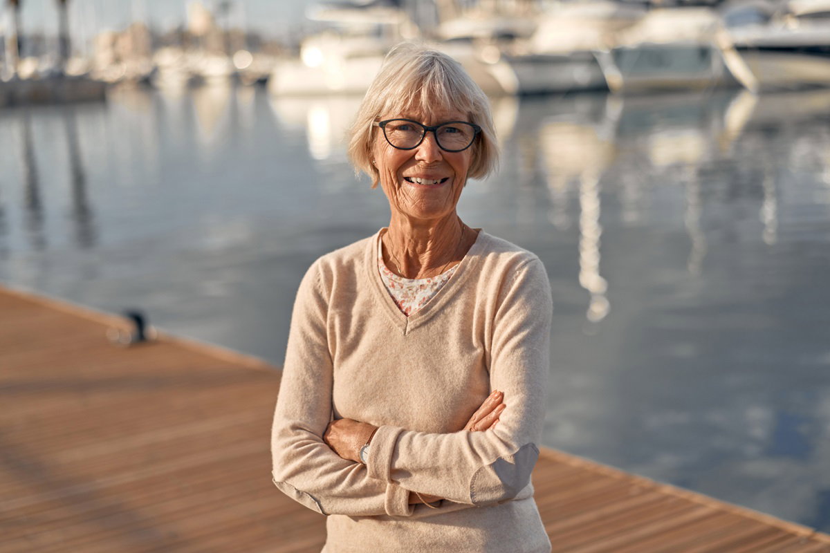 opalona seniorka w okularach stoi na nadmorskim pomoście