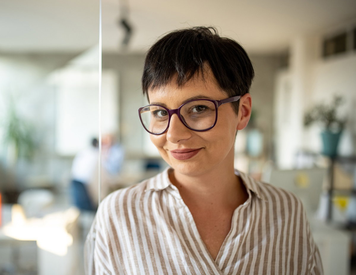 młoda kobieta w okularach i z krótkimi włosami uśmiecha się w biurze