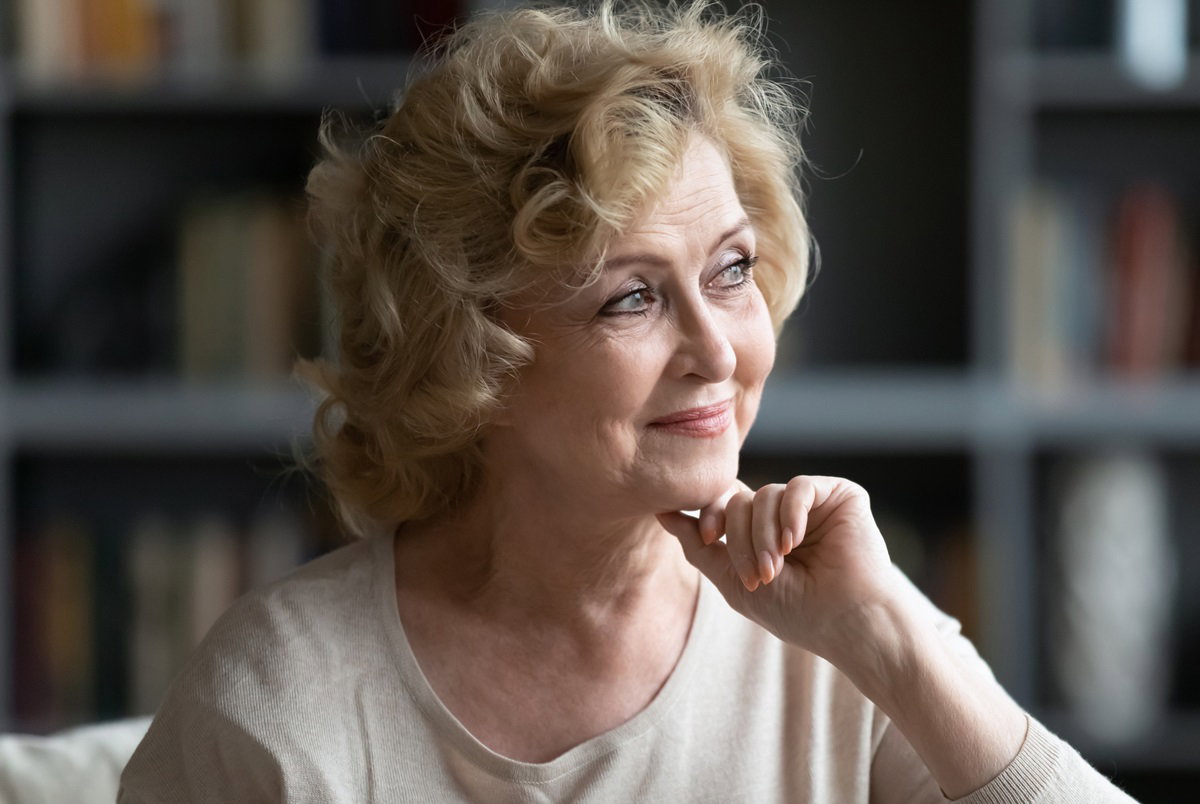 dojrzała kobieta z blond lokami patrzy zalotnie w dal rozmarzonym wzrokiem